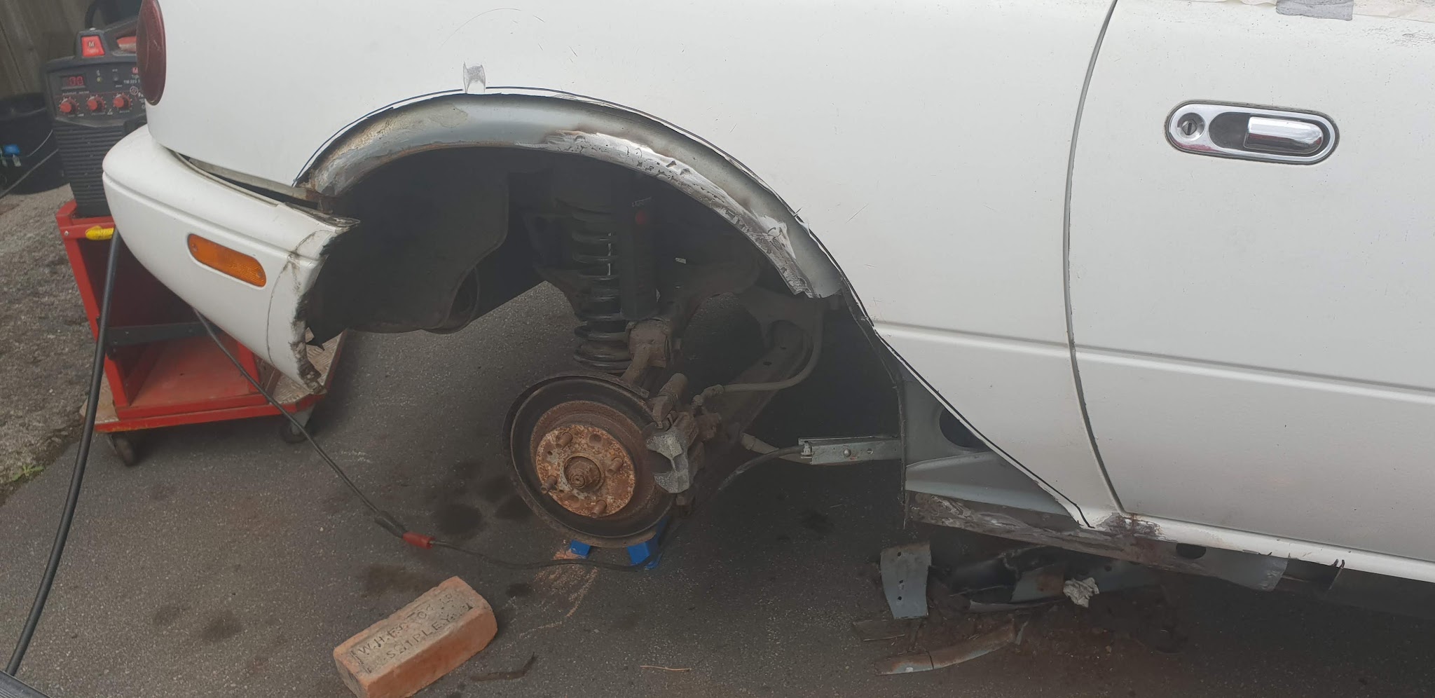 A white car with its wheel removed during repair work